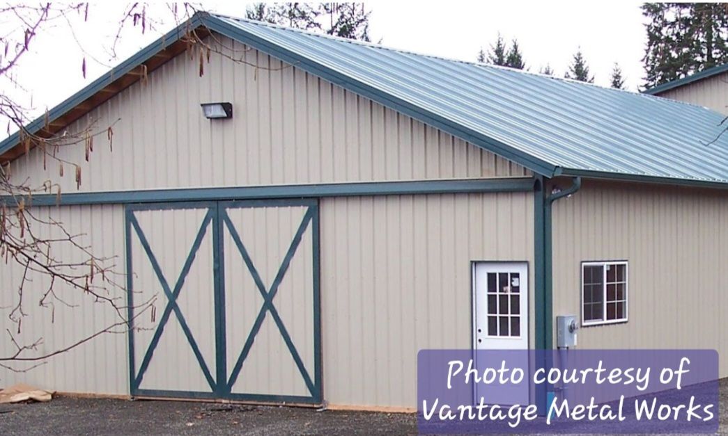 A beige metal building with a green roof, large sliding double doors, a white entry door, and a single window.