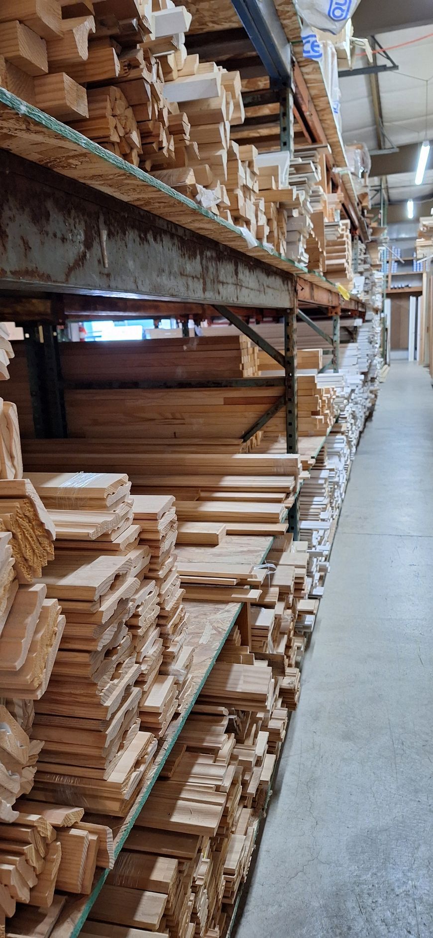 Rows of stacked wooden lumber boards on metal shelving in a warehouse aisle