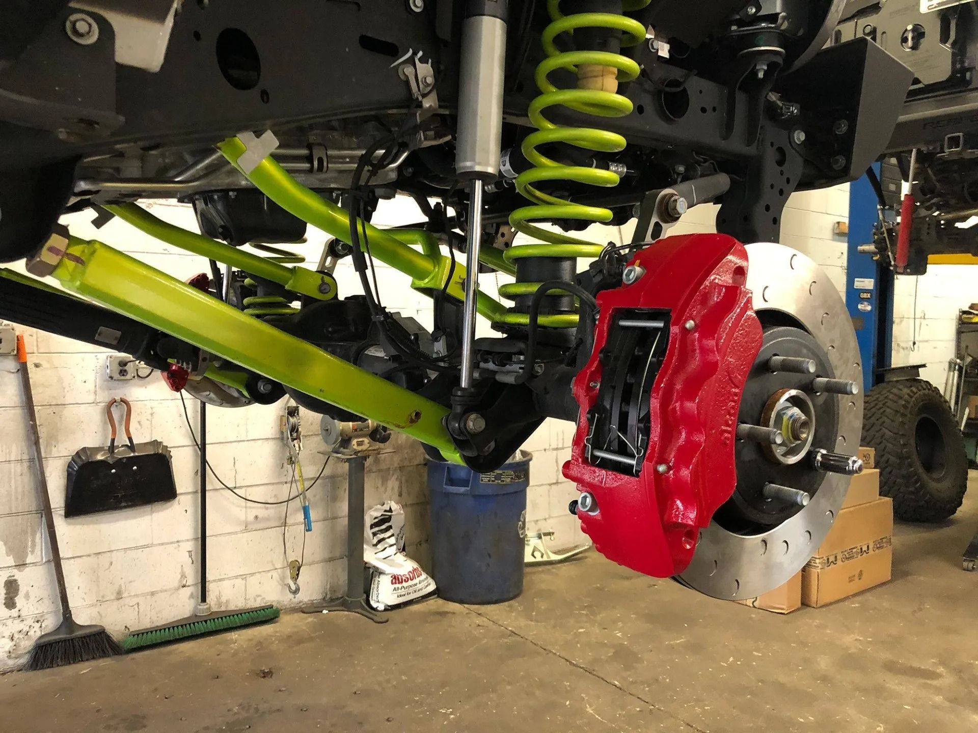 A Jeep's lifted suspension system with neon green control arms, a red brake caliper, and a coiled spring.