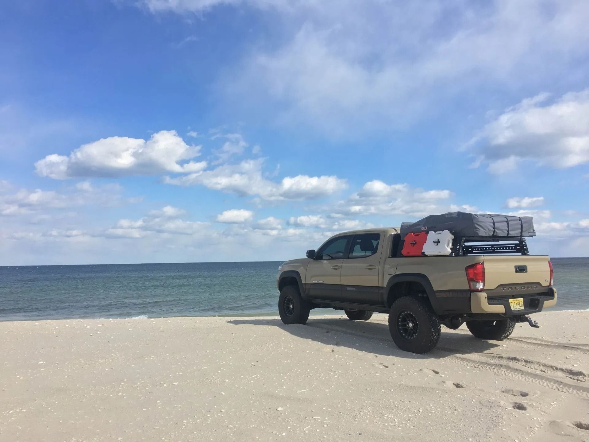 Tan pickup truck parked on a sandy beach, with a blue sky and ocean in the background.