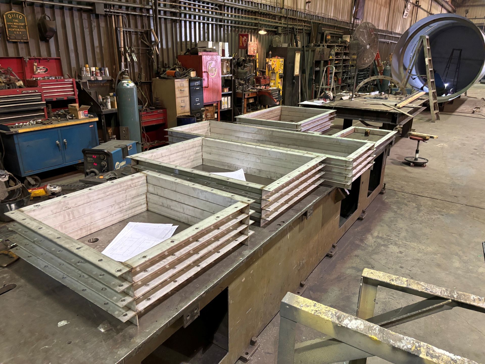 Large metal bins on a workbench in an industrial workshop with tools and equipment nearby