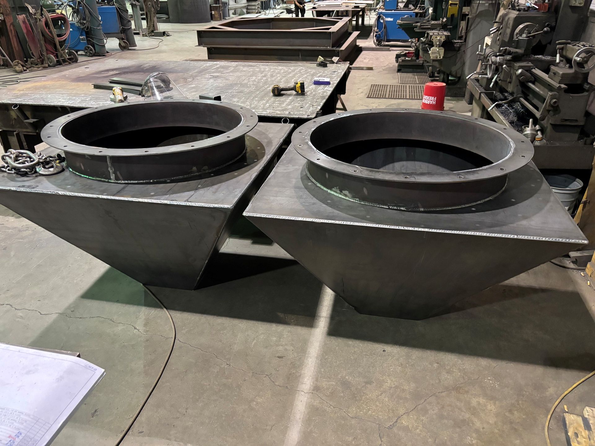 Two black metal hoppers with circular openings in an industrial workshop.