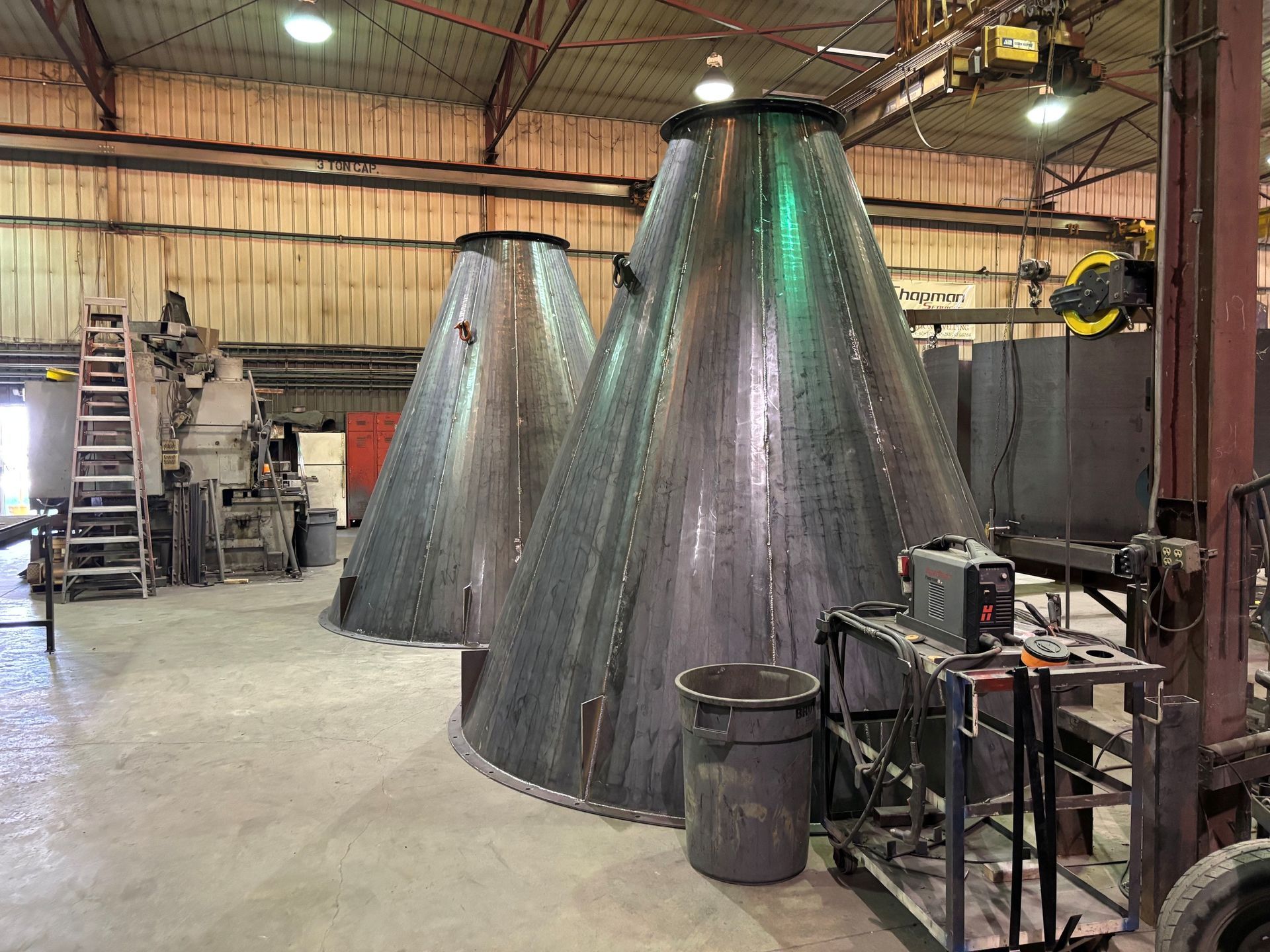 Industrial workshop with two large metal cone-shaped structures and machinery in the background