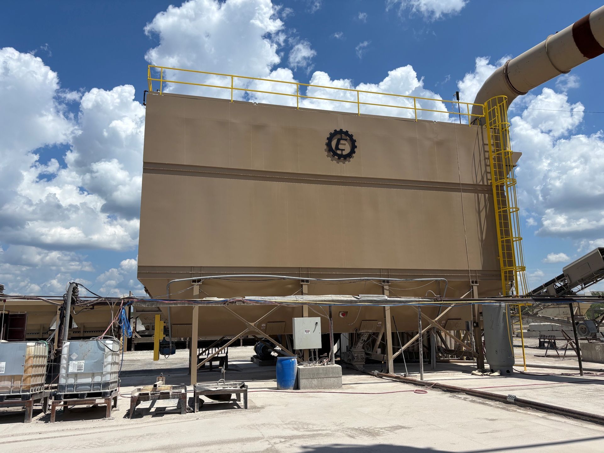 Large beige industrial silo or tank on scaffolding under a bright blue sky with clouds