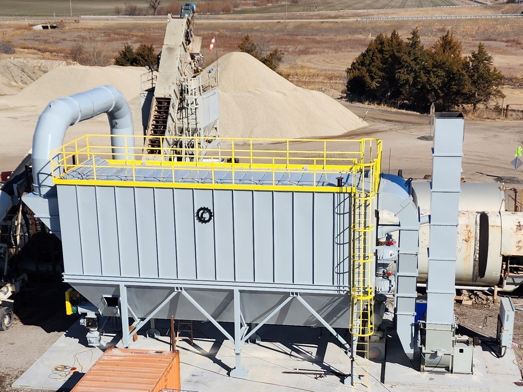 An aerial view of a factory with a large pile of sand in the background.