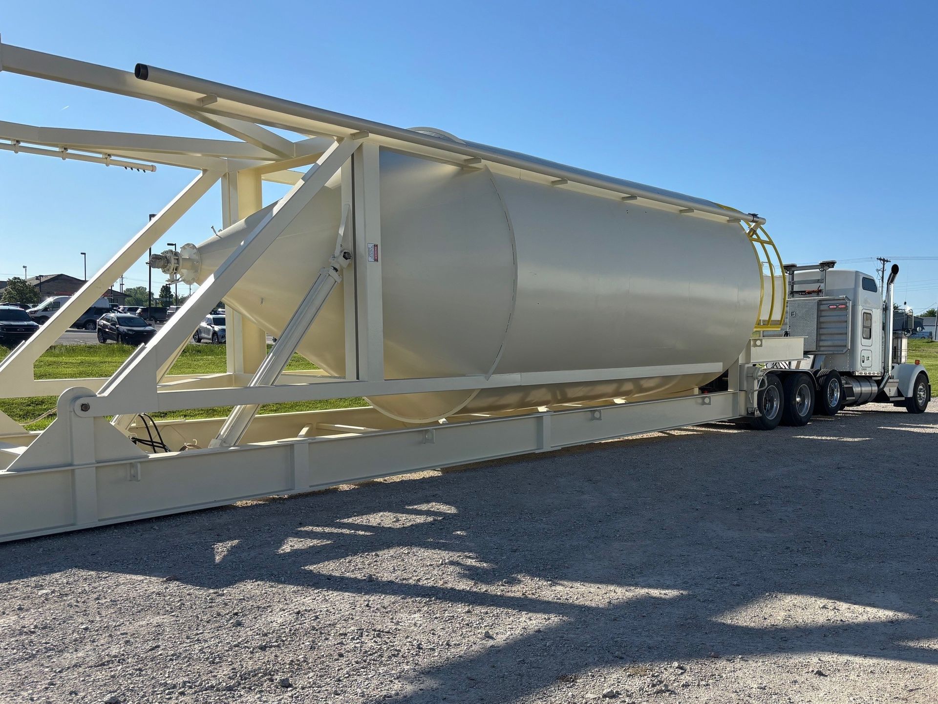 A white semi truck is carrying a large white tank on a trailer.