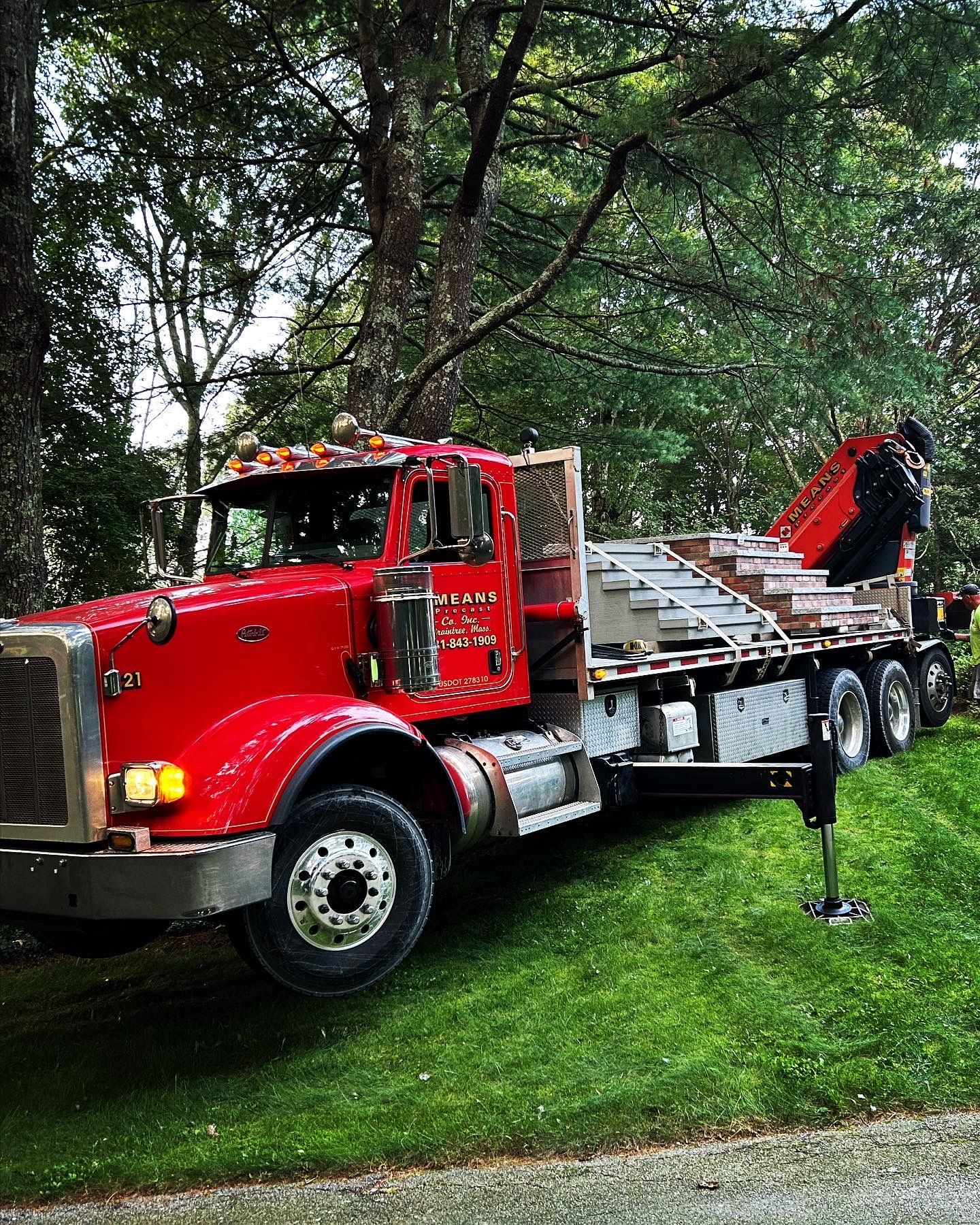 A red semi truck with a crane on the back is parked in the grass