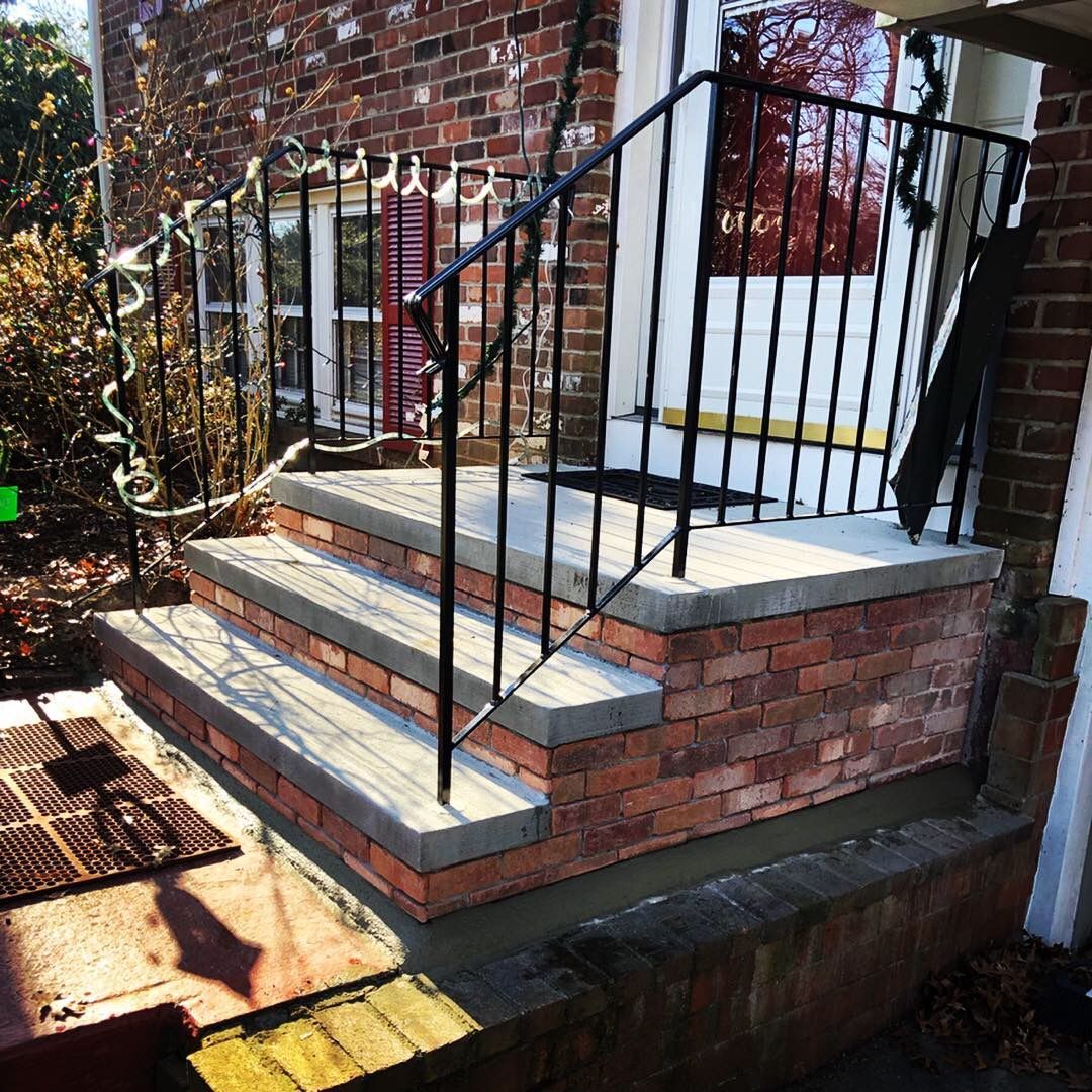 A brick porch with stairs and a wrought iron railing.
