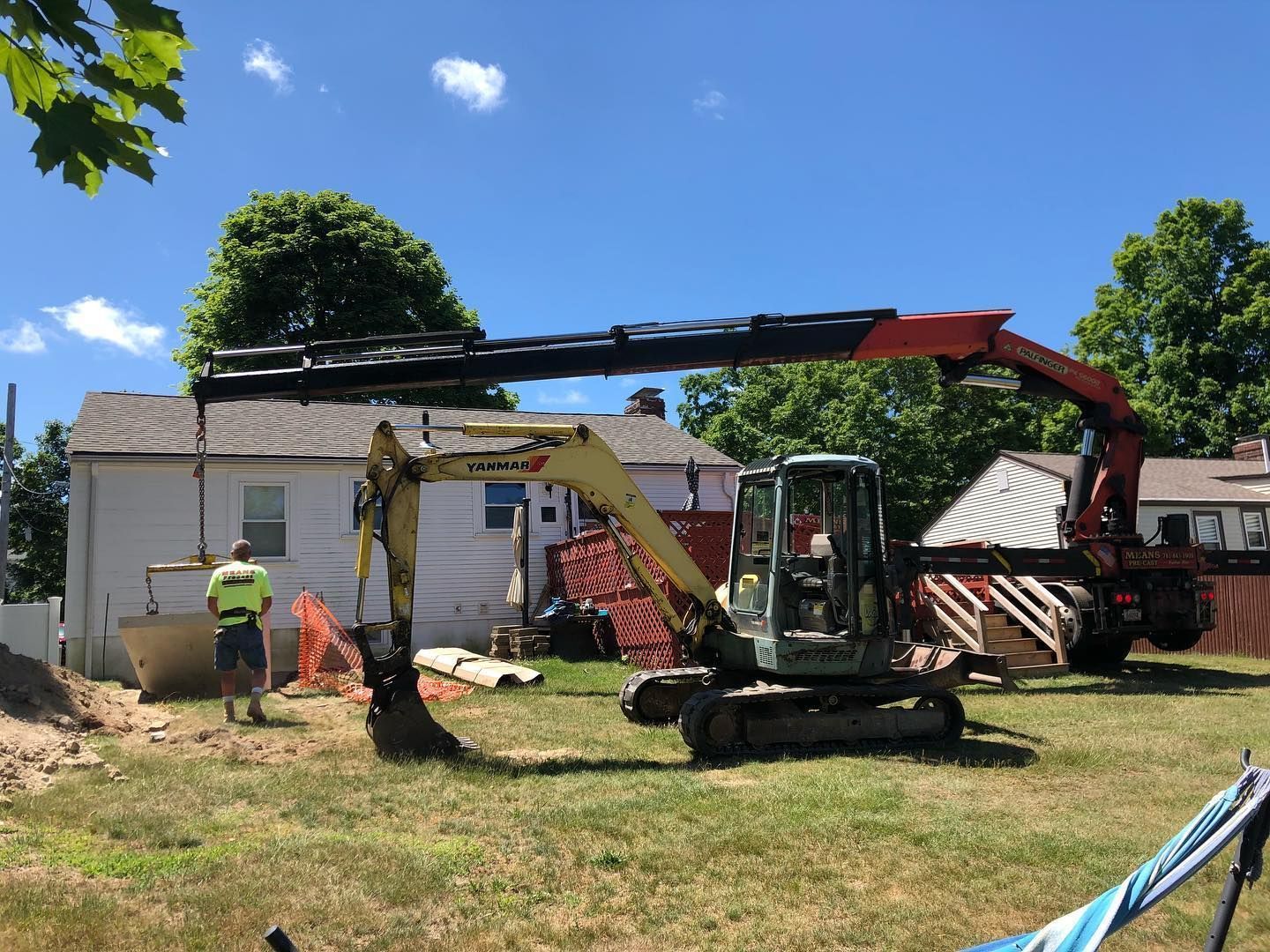 An excavator is being used to dig a hole in the grass in front of a house.