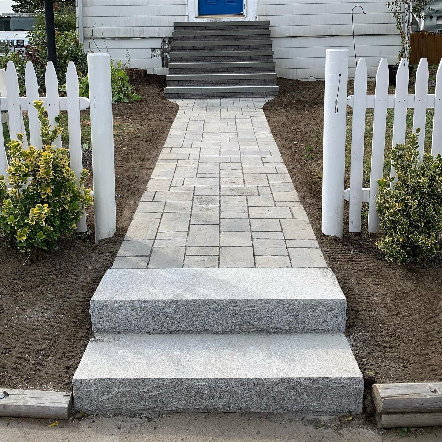 A white picket fence surrounds a stone walkway leading to a blue door