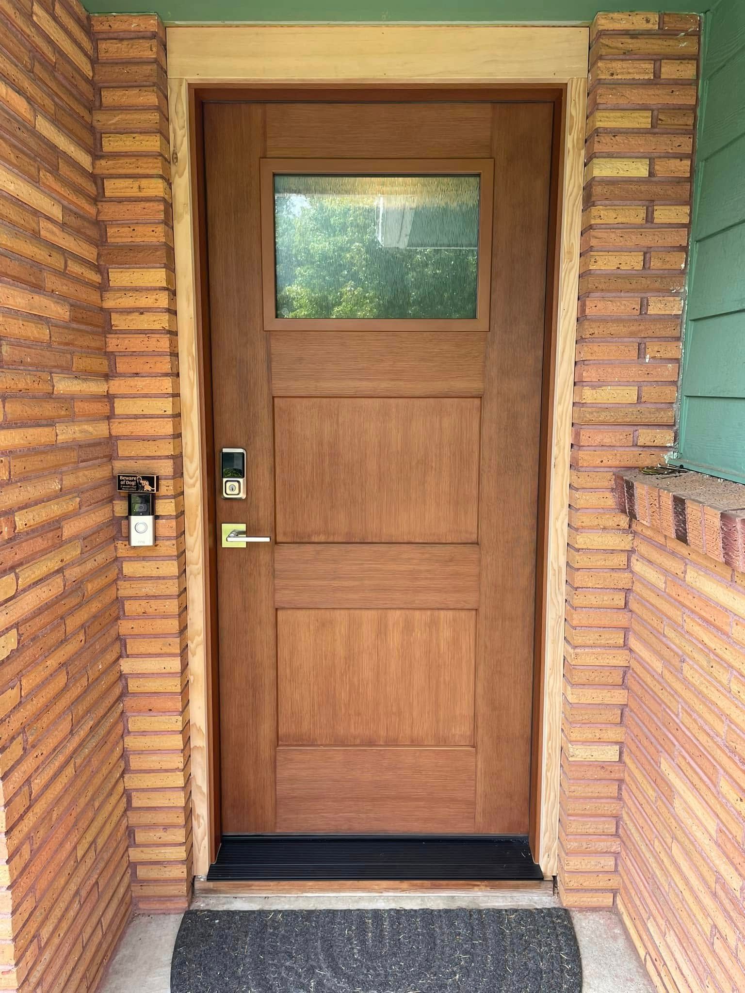 Wooden front door with glass panel and brick frame, door has a doorknob and keypad.