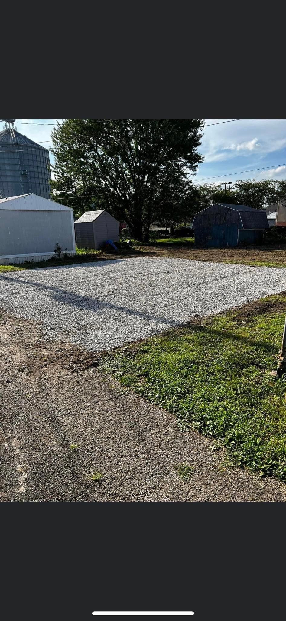 A gravel driveway leading to a building with a silo in the background.