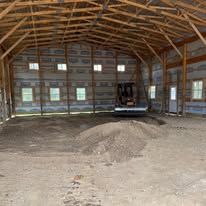 An empty barn with a pile of dirt in the middle of it.