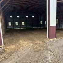 A large empty barn with a lot of windows and a dirt floor.