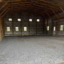 A large empty barn with a gravel floor and wooden beams.