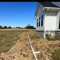 A white house is sitting on top of a dirt hill next to a field.