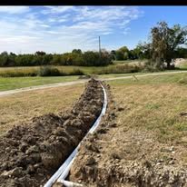 A pipe is being installed in the dirt in a field.
