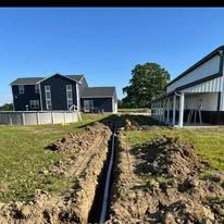 A pipe is being installed in the dirt in front of a house.