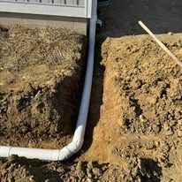A white pipe is being installed in the dirt next to a house.