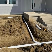 A drain pipe is being installed in the dirt in front of a house.