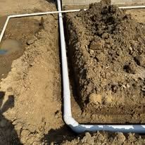 A pipe is being installed in the dirt next to a pile of dirt.