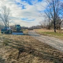 A truck is parked on the side of a dirt road next to a tractor.