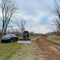 A truck is parked on the side of a dirt road next to a bulldozer.