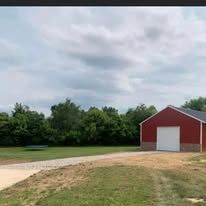 A red barn with a white door is sitting in the middle of a grassy field.