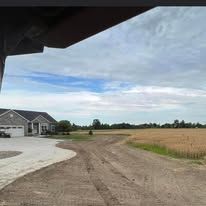 A house is sitting on the side of a dirt road next to a field.