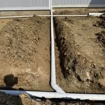 A white pipe is being installed in the dirt next to a house.