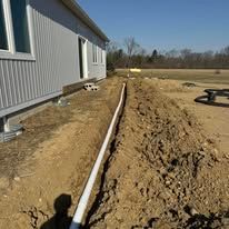 A white pipe is laying in the dirt in front of a house.