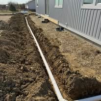 A drain pipe is being installed in the dirt next to a house.