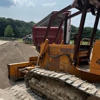 A yellow bulldozer is parked next to a red dumpster.