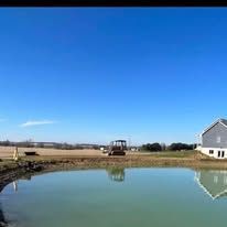 There is a pond in the middle of a field with a house in the background.