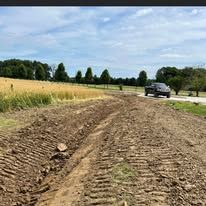 A truck is driving down a dirt road next to a field.