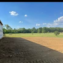 A large dirt field with trees in the background and a building in the foreground.