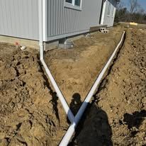 A pipe is being installed in the dirt next to a house.