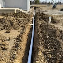 A white pipe is being installed in the dirt next to a house.