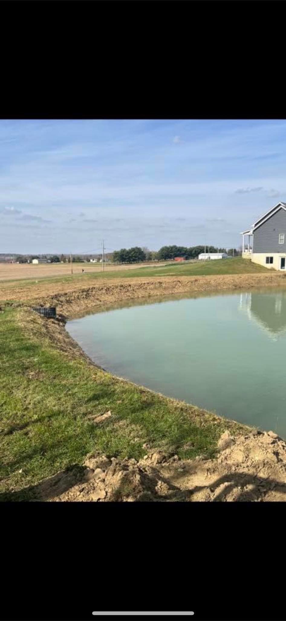 A small pond in the middle of a grassy field with a house in the background.