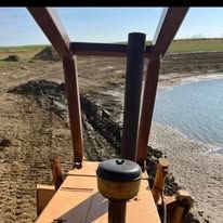 A bulldozer is driving down a dirt road next to a body of water.