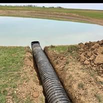 A large pipe is sitting in the dirt next to a body of water.