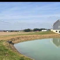 There is a pond in the middle of a field next to a house.