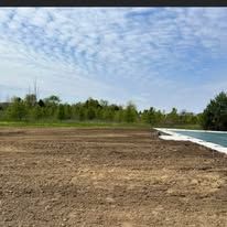 A large dirt field with a swimming pool in the background.