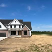 A large white house with a black roof is sitting on top of a dirt field.