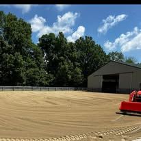 A red tractor is plowing a dirt field in front of a building.
