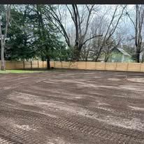 A large dirt field with a wooden fence and trees in the background.