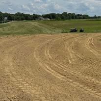 A dirt road going through a field with a tractor in the background.