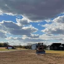A bulldozer is sitting in the middle of a dirt field in front of a house.