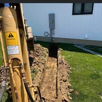 A yellow excavator is digging a hole in the ground in front of a house.