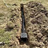 A drain pipe is being installed in the dirt in a field.
